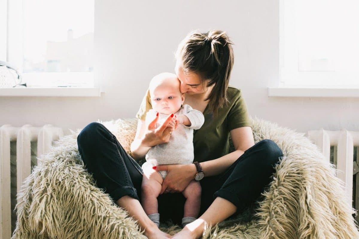 A young mother carrying her child while sitting in a furry cushioned sofa