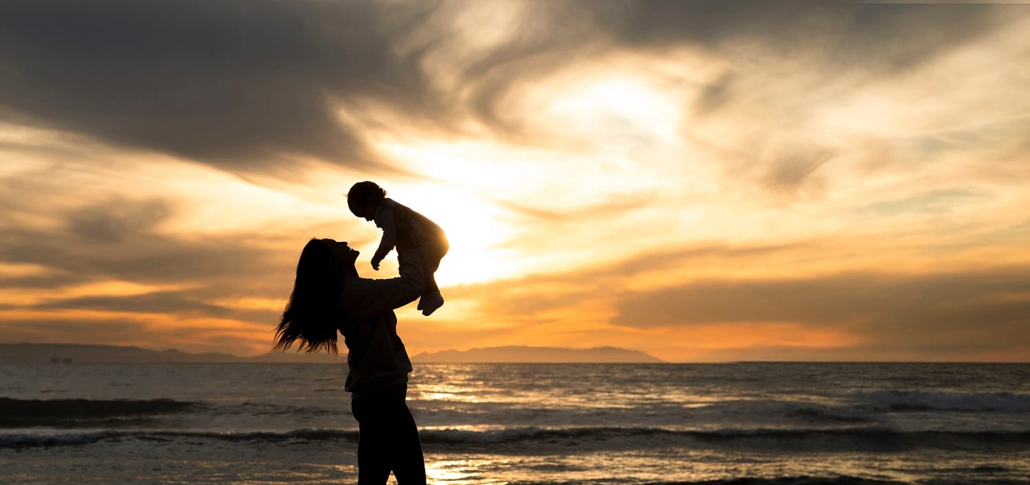 mother lifting her child up with the sunset and ocean in the background