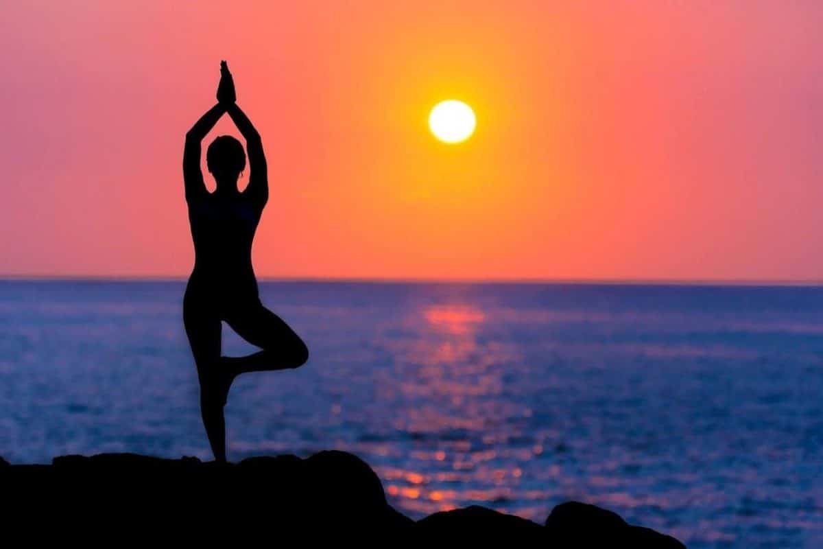 woman doing yoga exercise in front of a vast ocean and the setting sun