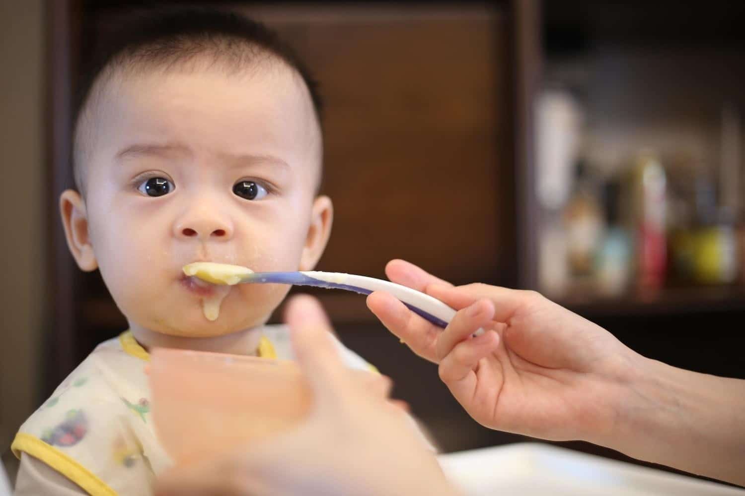 baby with a spoon full of baby food in his mouth